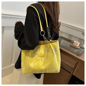 Detalle del bolso tote amarillo con patrón de diamantes y correa de cadena dorada