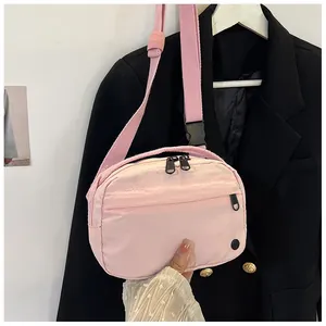 Close-up of a light pink casual crossbody bag with wide fabric strap and zippers