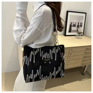 Détail du sac cabas en toile noire avec broderie ondulée et bandoulière chaîne dorée