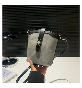 Detailed view of grey canvas bucket bag with black leather trim and golden metal lock