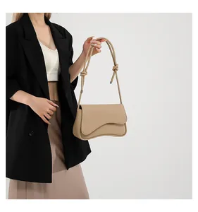 Detail of beige French-style shoulder bag with knotted strap and curved flap design