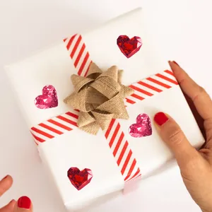 Pegatinas de gemas de corazón rojas y rosas decorando una caja de regalo blanca con lazo