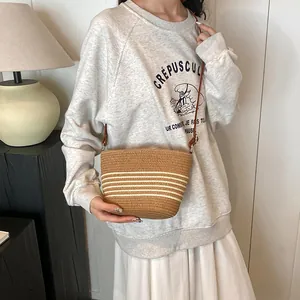 Straw woven bucket bag with white stripes and brown leather strap for beach vacations
