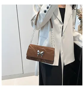 Close-up of brown crinkled leather shoulder bag with silver butterfly buckle and chain strap