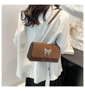 Detail of a brown pleated leather bag featuring a silver butterfly buckle and chain strap