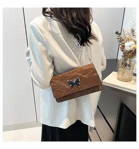 Close-up of brown textured leather shoulder bag with chic butterfly buckle and chain