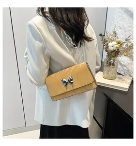 Detail of yellow leather shoulder bag featuring silver butterfly buckle and chain strap