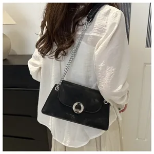 Sac bandoulière vintage noir avec chaîne, porté sur un chemisier blanc élégant