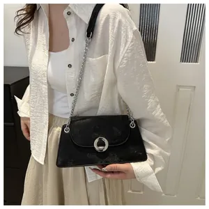 Détail d'un sac bandoulière noir avec boucle argentée et chaîne porté par un mannequin