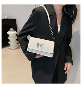 Detail of white leather shoulder bag with silver bow clasp on black blazer outfit
