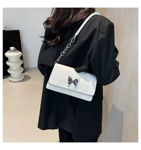 Detail showing white leather shoulder bag with metallic bow buckle and chain strap