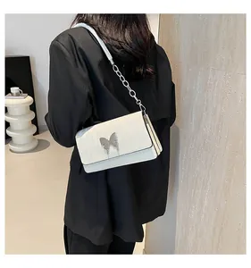 Detail of white pleated shoulder bag with silver butterfly buckle on black blazer