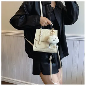 Detail van crème crossbodytas met metalen gesp en een witte pluchen wolkenhanger opzij