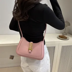 Pink minimalist shoulder bag with gold geometric clasp shown on a white cabinet