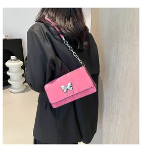 Detail of pink glossy shoulder bag with silver bow buckle on model's black suit jacket