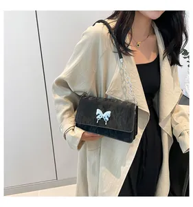 Detail of black textured shoulder bag featuring silver butterfly buckle and chain strap