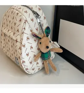 Detail of cream backpack featuring rabbit prints and a cute plush bunny charm on the side
