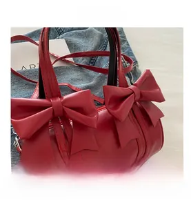 Detail view of red barrel handbag featuring large bows and gold fashion lettering