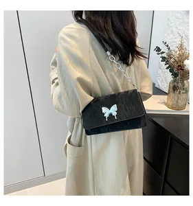 Black crinkle textured shoulder bag with silver butterfly charm on a trench coat model