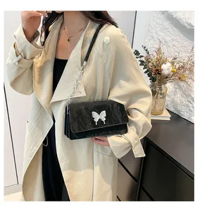 Detail of black bow shoulder bag featuring a silver butterfly metallic piece and pleated texture