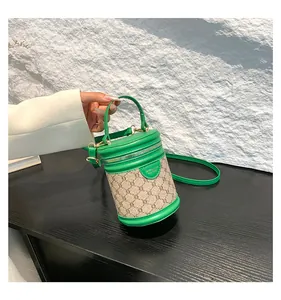 Detail showing green leather piping and beige floral fabric on a cylinder bucket bag