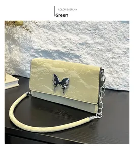 Detail view of light green wrinkled patent leather bag with silver butterfly ornament