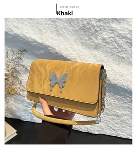 Close-up of khaki shoulder bag featuring textured leather and a silver metal butterfly