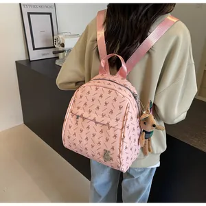 Pink backpack with rabbit print and plush charm shown on model in modern interior