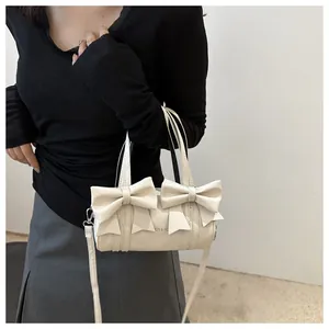 Detailed view of the large decorative bows on the cream-colored cylinder handbag