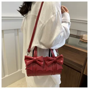 Detail of red cylindrical shoulder bag with large bows and embossed lettering