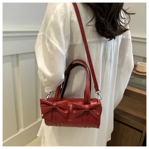 Detail shot of a red cylindrical shoulder bag featuring oversized bow accents and silver hardware