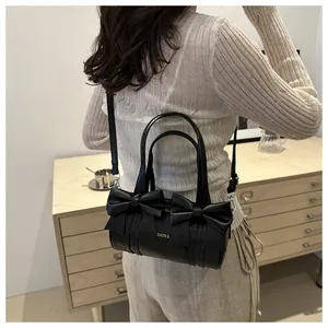 Detail of a black cylinder bag featuring oversized bows and detachable shoulder strap