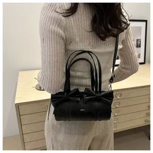 Chic black cylindrical bag with large bows and gold lettering shown on a model