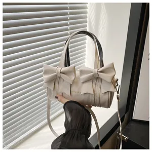 Detail of cream white cylinder bag with bow accents and gold Fashion & H lettering