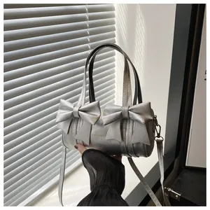 Detail view of metallic silver cylinder bag with large bows and Fashion & B logo text