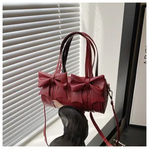 Detail of dark red cylindrical shoulder bag with elegant bow accents and gold fashion logo
