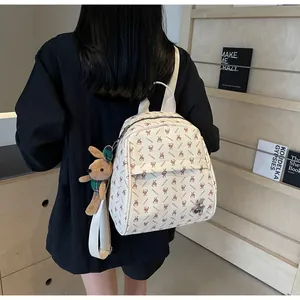 Close-up of beige backpack with brown rabbit prints and plush charm on wood shelf
