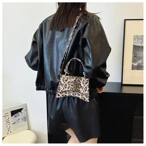 Detail of leopard print handbag with curved base and adjustable shoulder strap shown on model