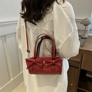 Red cylinder shoulder bag with bow details and golden text on model for fashion look