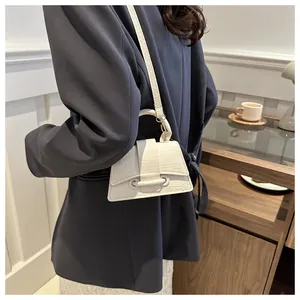 Model draagt een witte mini-crossbodytas met krokodillenpatroon en ronde handgreep