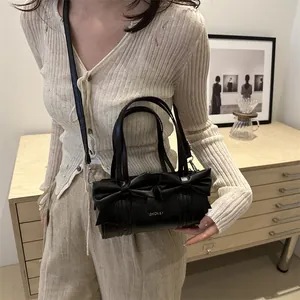 Black cylindrical shoulder bag with bow accents and adjustable strap in lifestyle setting
