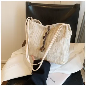 Detail of beige pleated tote bag featuring woven knot and brown bead accessory