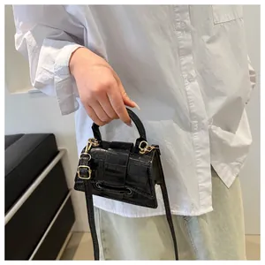 Detail van zwarte mini-crossbodytas met krokodillenpatroon en gouden hardware afwerking