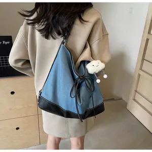 Detail of blue denim tote bag with black leather base and decorative side bow