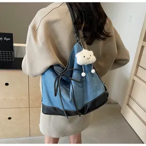 Detail of blue denim tote bag with black leather contrast and plush cloud keychain charm