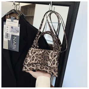 Detail of leopard print handbag featuring a curved base and adjustable shoulder strap