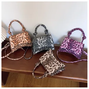 Detail view of four leopard print handbags in various colors on a dark wooden table