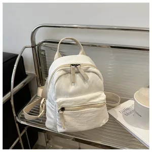 Detail of a minimalist off-white canvas backpack showing front zipper and top handle