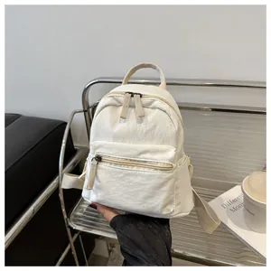Close-up of a mini white canvas backpack with zip pockets and adjustable straps in a studio set