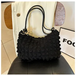 Detail of black bubble textured shoulder bag with slim straps on a leather chair